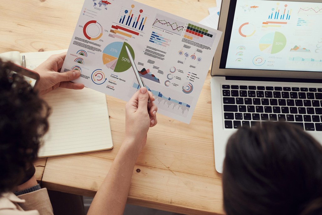 To personer sidder ved et skrivebord. Den ene person har et papir i hånden, som den anden person peger på med en kuglepen.