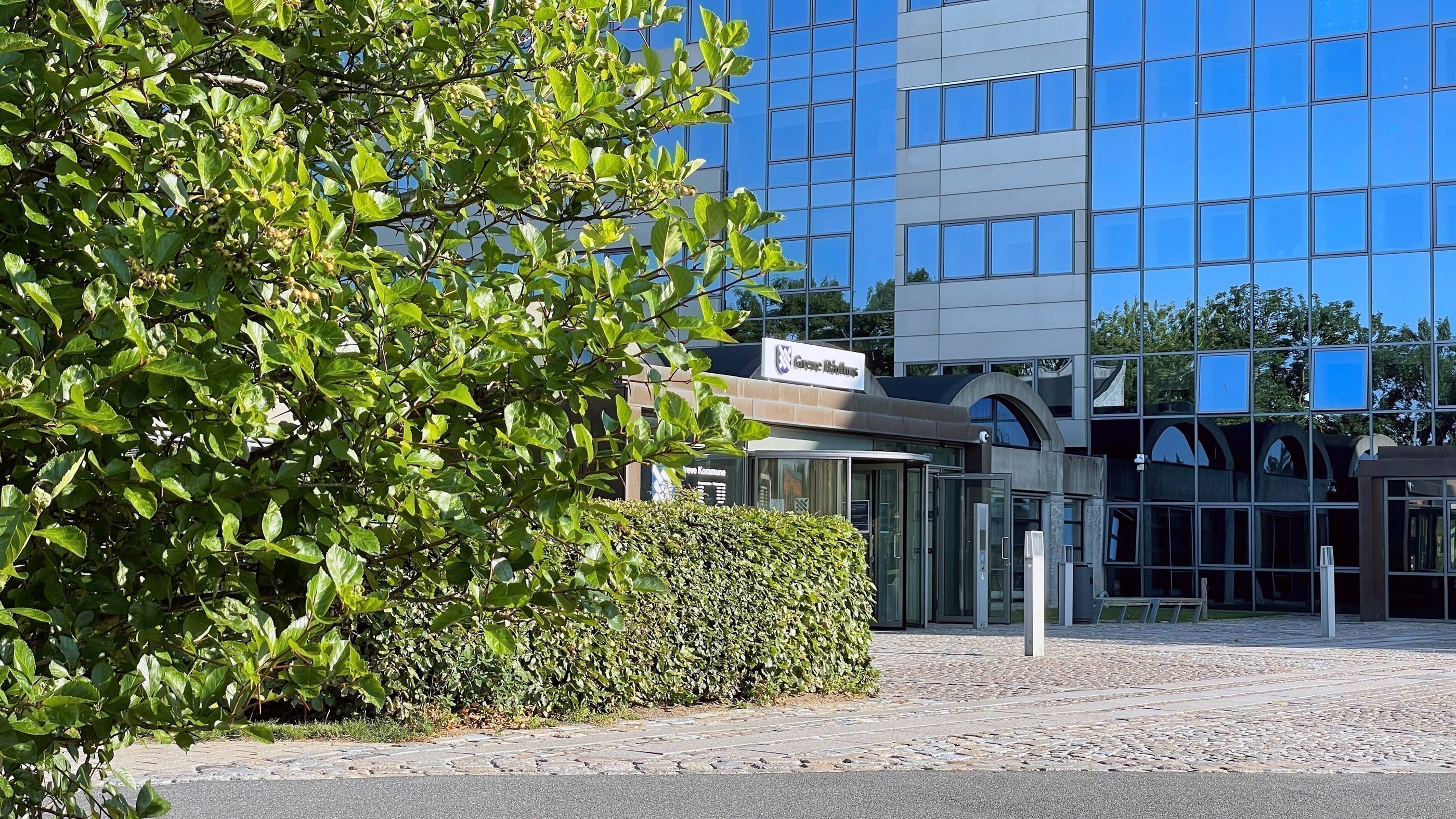 Hovedindgang til Greve Rådhus med træer og buske i forgrunden