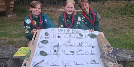 Tre spejdere der sidder med et stort stykke papir hvor der står "natur-bingo", og der er fundet ting fra naturen til hvert bogstav.