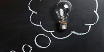 Sort tavle med en tankebobbel tegnet med kridt. Inde i tankeboblen er der en lyspære