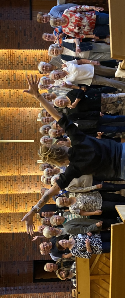 Gospelkoret Grace i Hundige kirke der står og synger og er glade, består primært af ældre mennesker. Forrest står der, med ryggen til, en meget energisk dirigent med armene over hovedet. Bagerst på væggen hænger et kors, da de er inde i kirken.