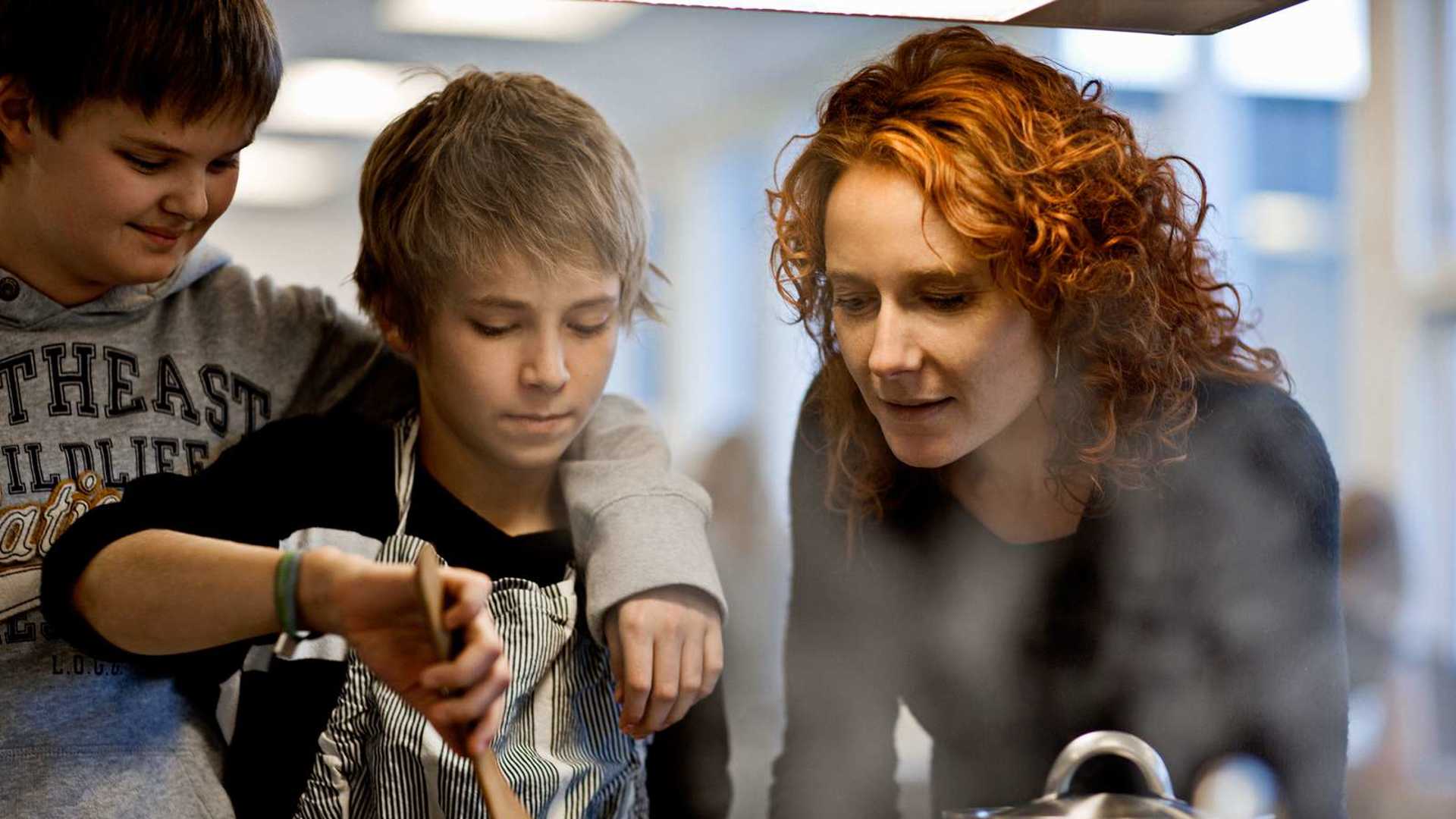 En kvinde med to drenge der står og rør i en gryde
