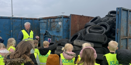 En skoleklasse der lytter til en mand fra miljøcenteret, der står ved en container fyldt med gamle dæk