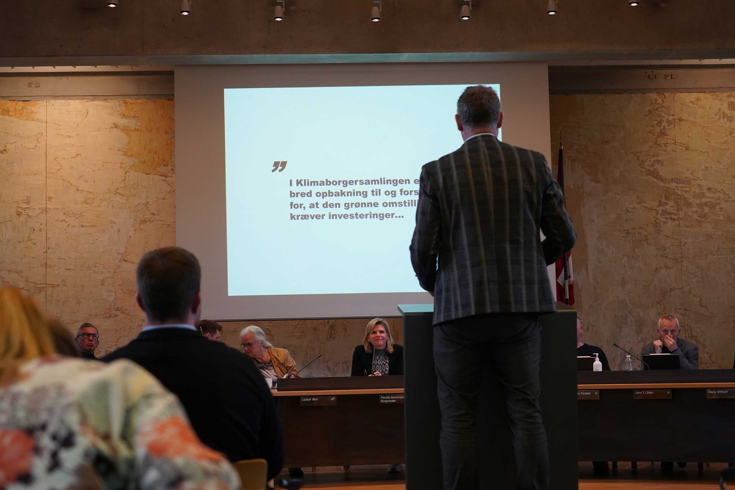 En mand står med ryggen til og præsenterer i Greve Kommunes byrådssal.