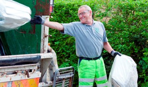 Smilende affaldsmedarbejder smider en affaldssæk op i skraldevogn. Smilende affaldsmedarbejder smider en affaldssæk op i skraldevogn.