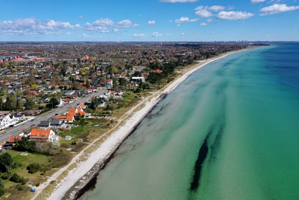 Luftfoto af Greve Strand. Til venstre ses by og strand. Til højre ses havet.