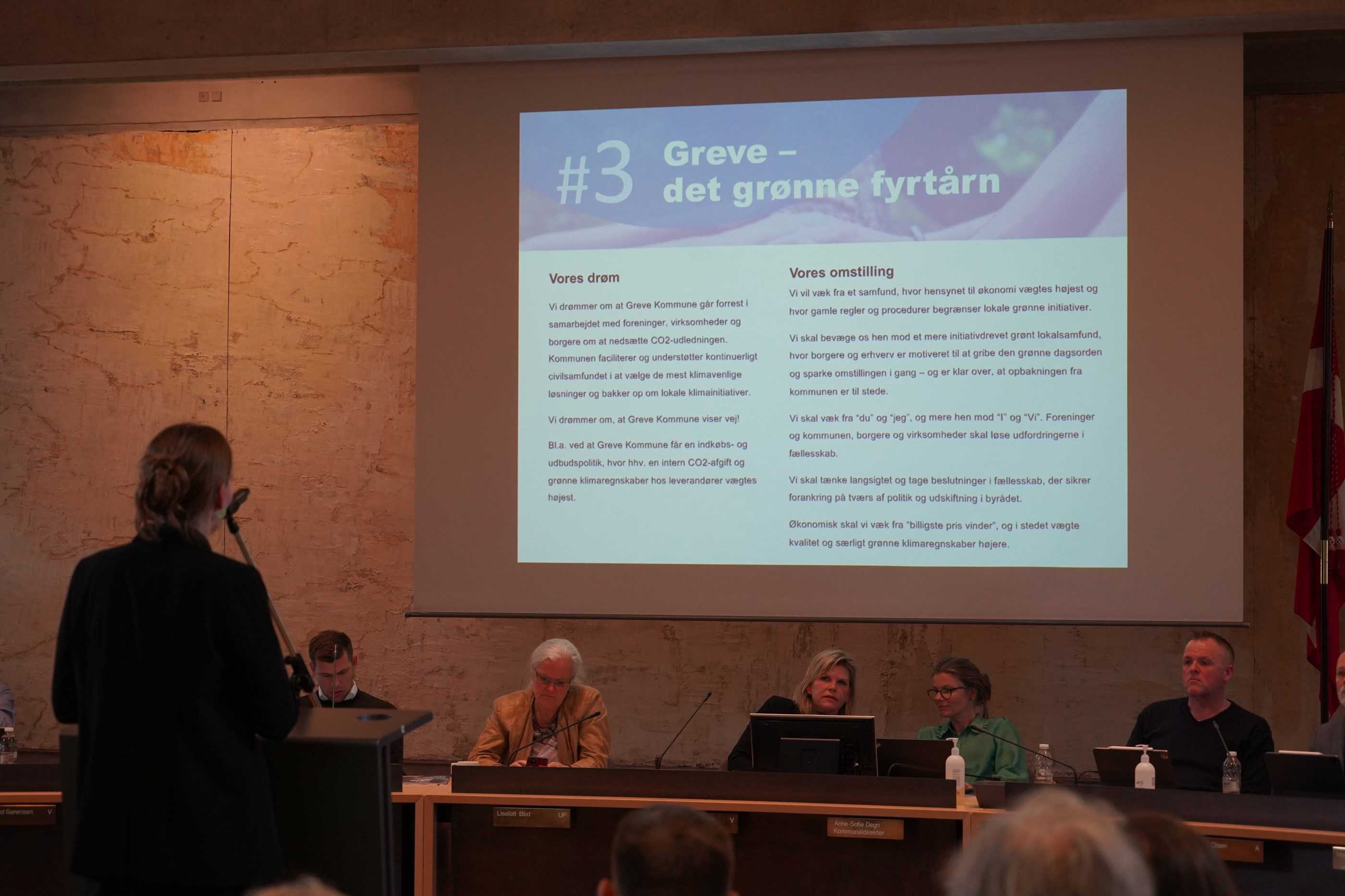Billede af en præsentation hvor der står "Greve - det grønne fyrtårn". En person står med ryggen til og præsenterer