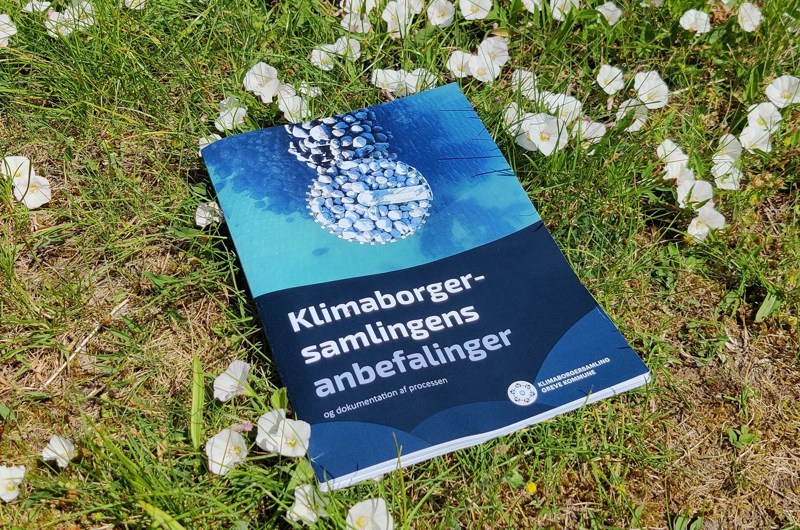 Samlet rapport med Klimaborgersamlings anbefalinger, liggende på et tæppe af græs og blomster.