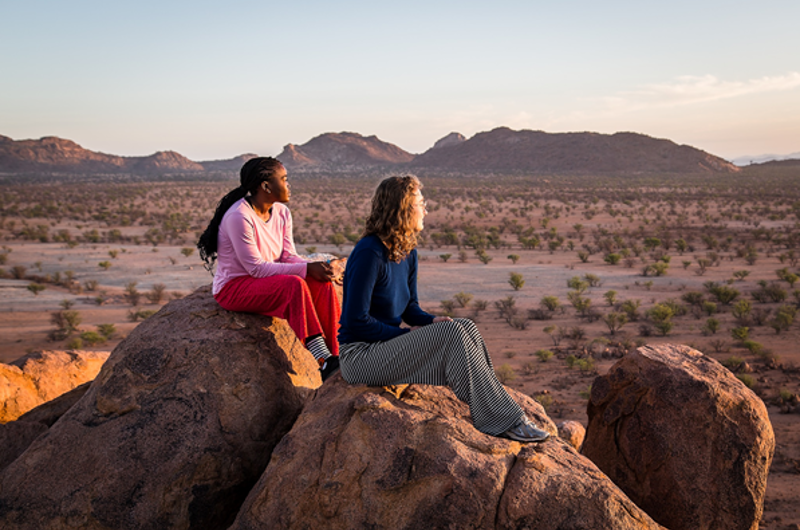 To unge kvinder der sidder og kigger ud over savannen i Afrika