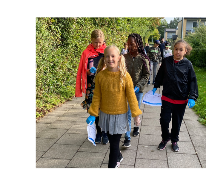 En gruppe børn med fire tydeligt i forgrunden. De er glade og går udenfor. De har alle sammen blå gummihandsker på hænderne.